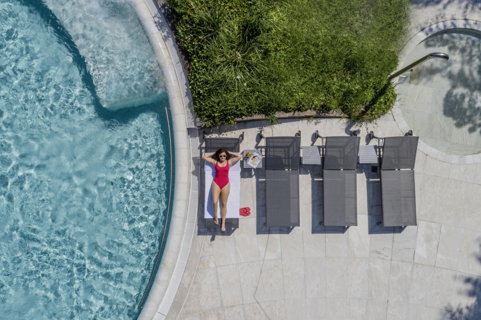 Frau in pinkem Badeanzug entspannt auf grauer Sonnenliege am Beckenrand der Caracalla Therme Baden-Baden, Sommeraufnahme.