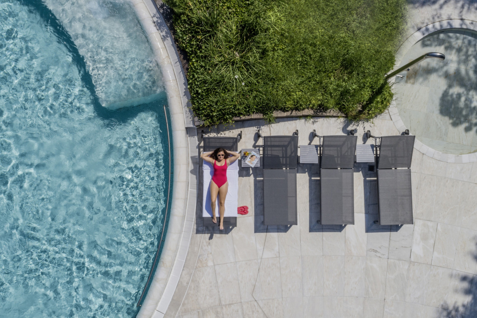 Frau in pinkem Badeanzug entspannt auf grauer Sonnenliege am Beckenrand der Caracalla Therme Baden-Baden, Sommeraufnahme.