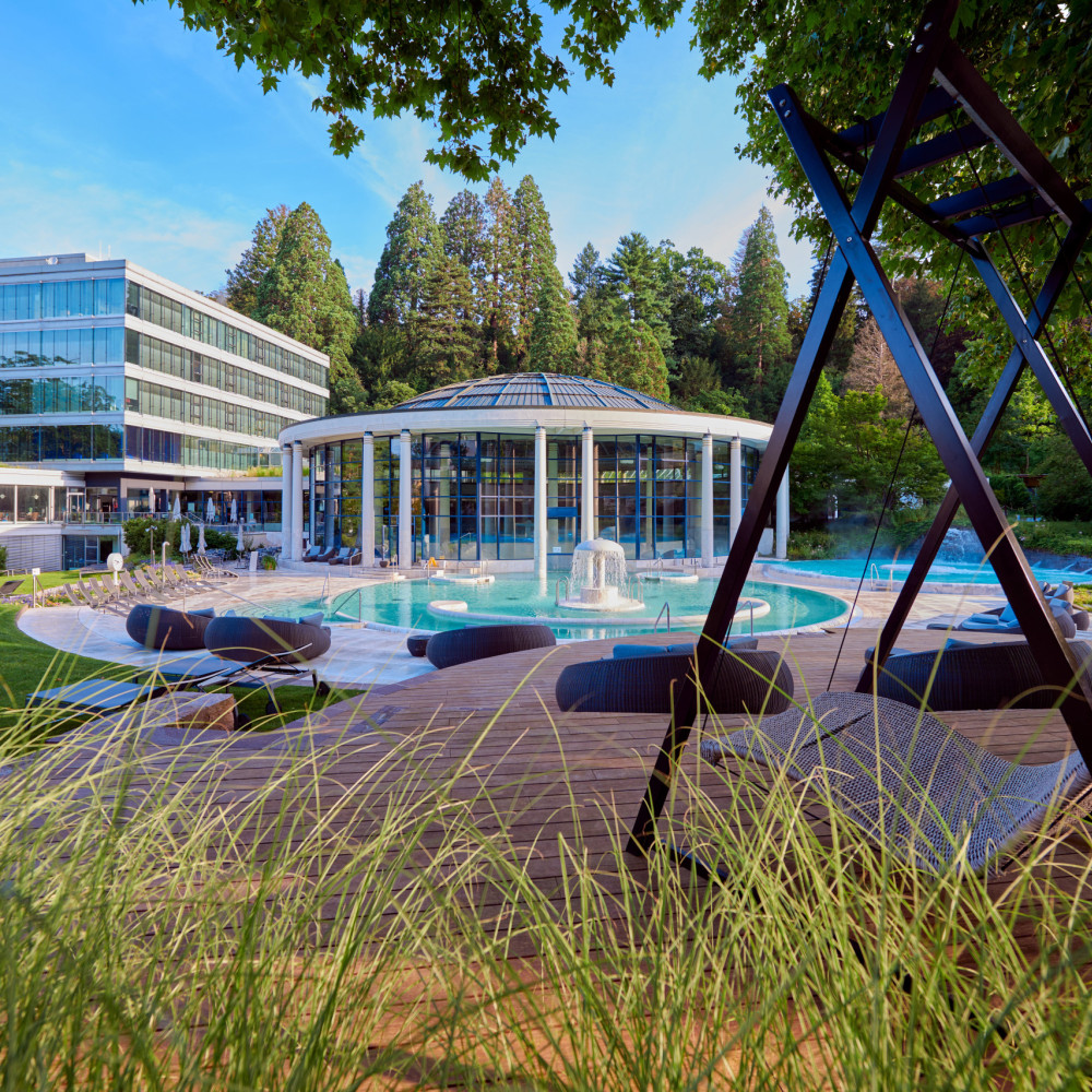 Caracalla Therme Baden-Baden mit Glasrotunde und Außenbecken, fotografiert durch Gräser im Vordergrund.
